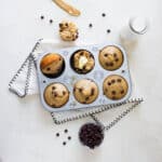 Top view of muffins in a muffin tin with one broke in half and butter on it.