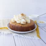 Small round cake with whipped cream and bananas on top, on a white plate.