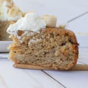 Slice of cake on a wooden spatula with whipped cream and bananas on top.