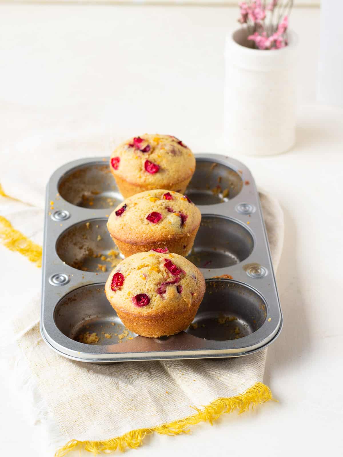 Three cranberry orange muffins setting on top of a muffin tin in the center.