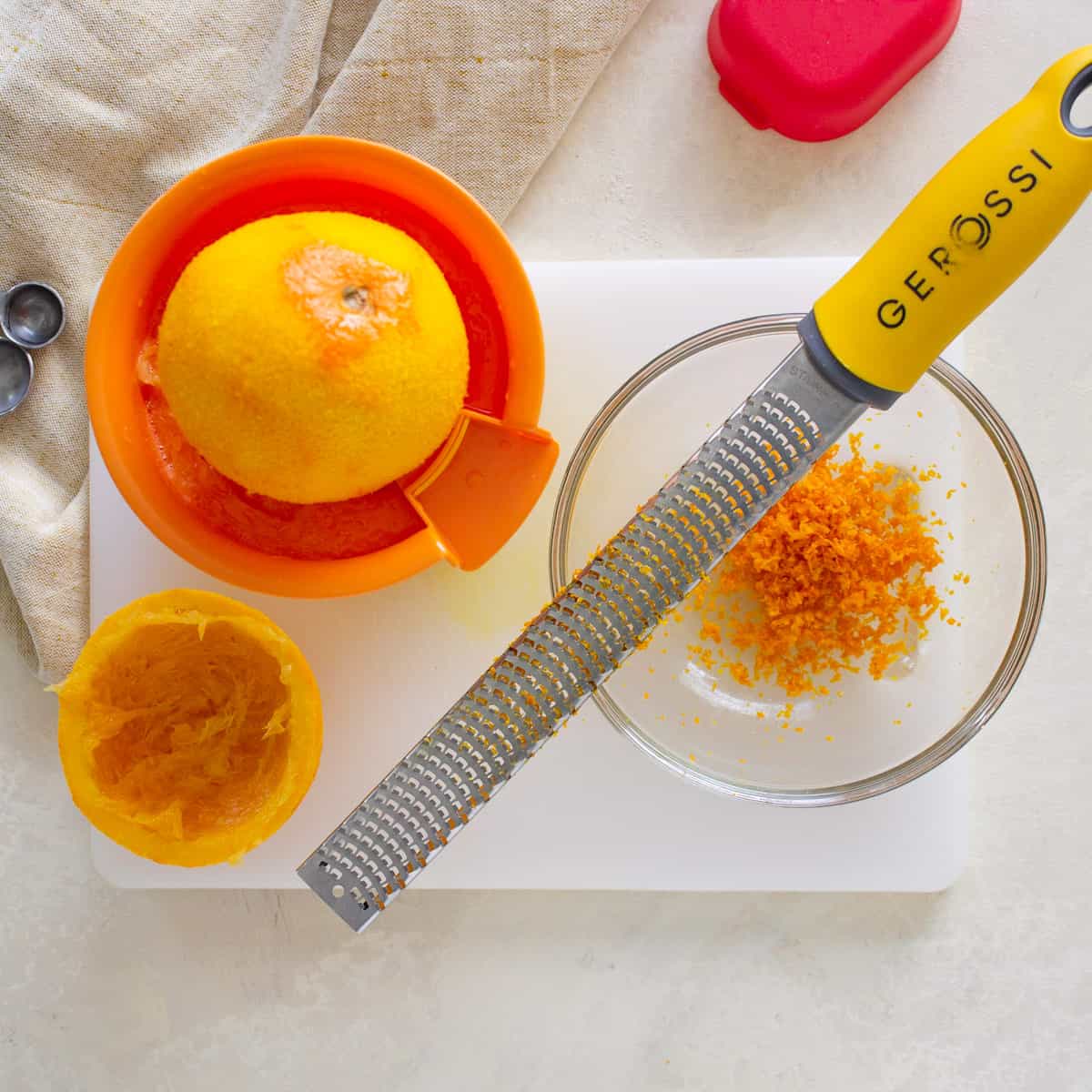 Orange zest in a small bowl with a microplane setting on top and, a zested orange half on a citrus juicer.