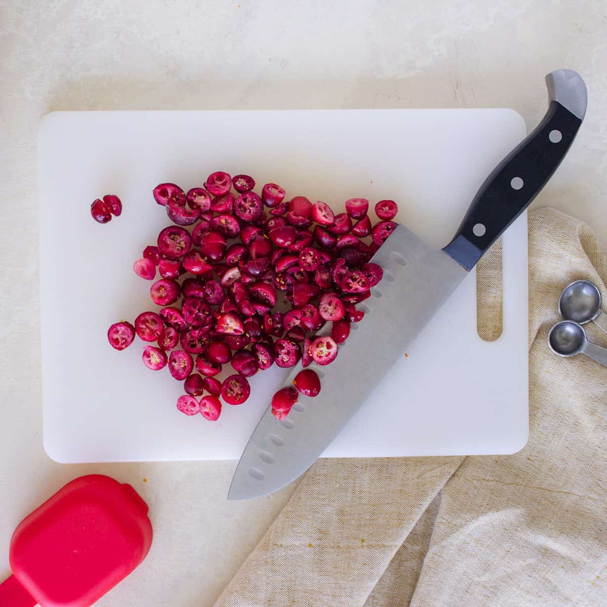 Chopped cranberries and a chef's knife on a white cutting board.