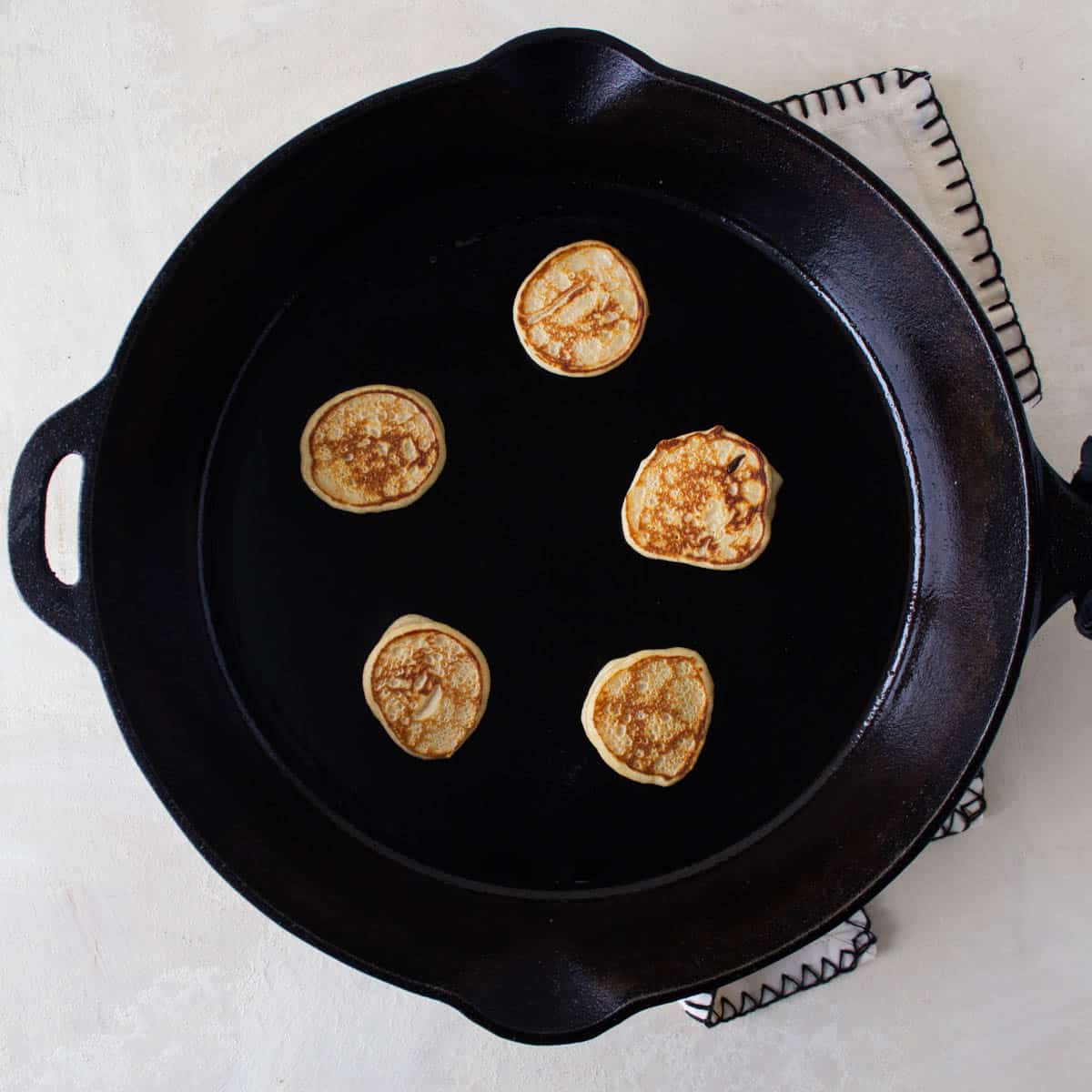 Mini pancakes cooking in a cast iron skillet.