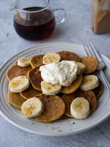 A plate of mini banana pancakes topped with whipped cream, sliced bananas and cinnamon.