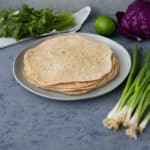 Cooked whole wheat tortillas on a plate with veggies around it.