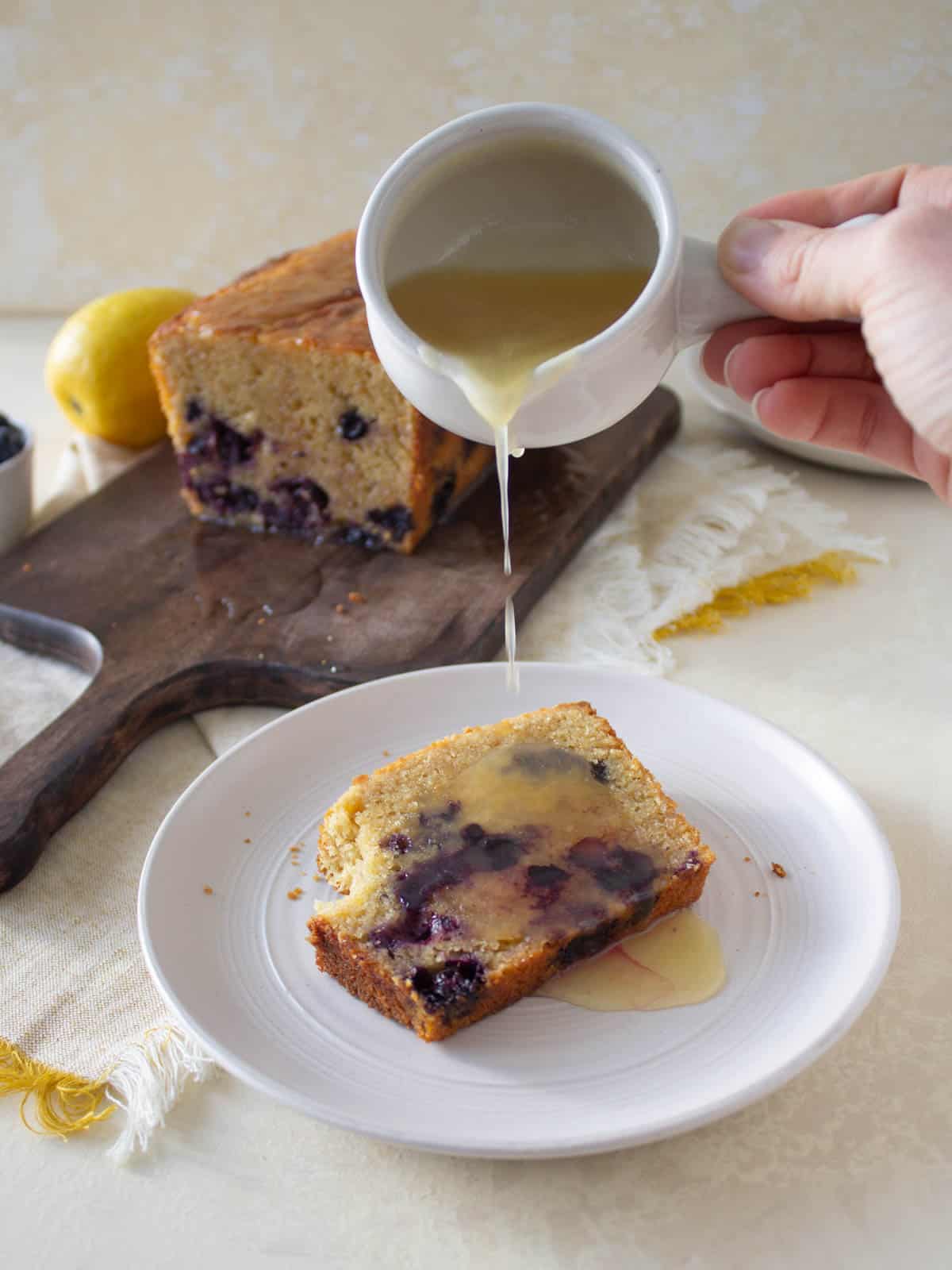 Pouring lemon glaze onto a slice of blueberry bread.