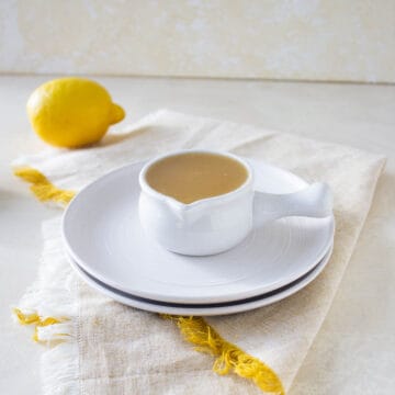 Lemon glaze in a white pouring cup sitting on a stack of plates.