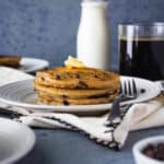 A short stack of whole wheat chocolate chip pancakes on a white plate with a pat of butter on top.