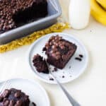 Piece of chocolate banana cake on a white plate with a bite of cake on a fork.