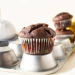 A chocolate muffin sitting on top of an upside down muffin pan.