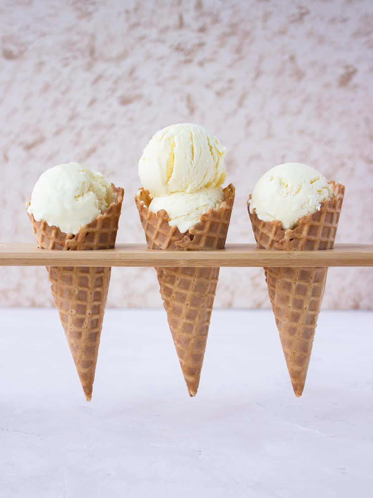 Straight on shot of three waffle cones with vanilla ice cream sitting in a wooden holder.