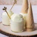 Mini mason jars full of vanilla ice cream with a stack of sugar cones next to them.