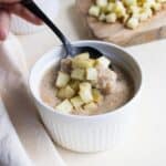 Scooping a spoonful of cracked wheat porridge topped with diced apples.