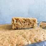 A piece of zucchini cake on a spatula on top of the sheet cake.