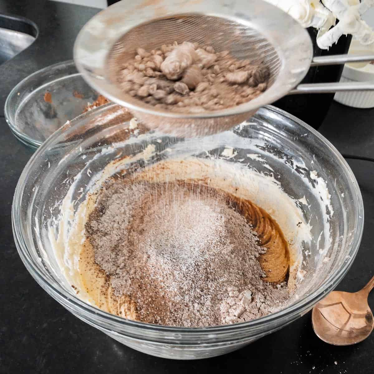 Sifting powdered sugar and cocoa powders into a bowl with cream cheese and butter.