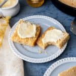 A piece of cornbread cut in half on a plate and spread with butter and honey.