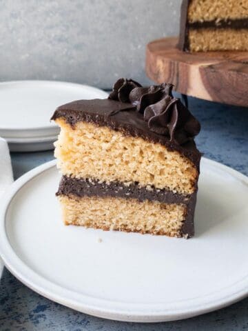 A slice of two layer vanilla cake with chocolate frosting on a plate.