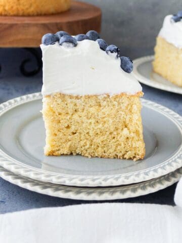 A slice of whole wheat sponge cake with whipped cream and blueberries on top.