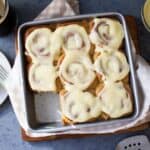 Cinnamon rolls with icing on top in a pan.