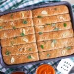 Breadsticks on a sheet tray with sliced garlic and herbs on top.