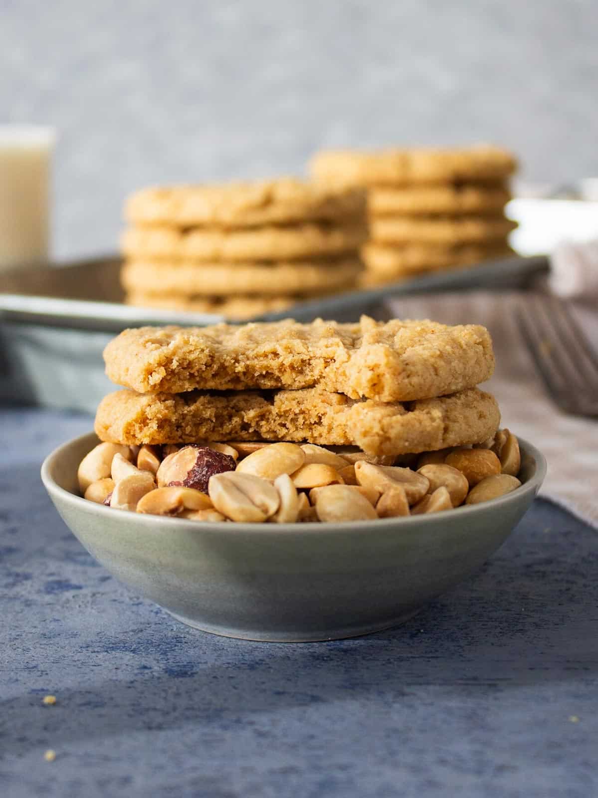 Two peanut butter cookies with bites taken out sitting on top of a small bowl of peanuts.