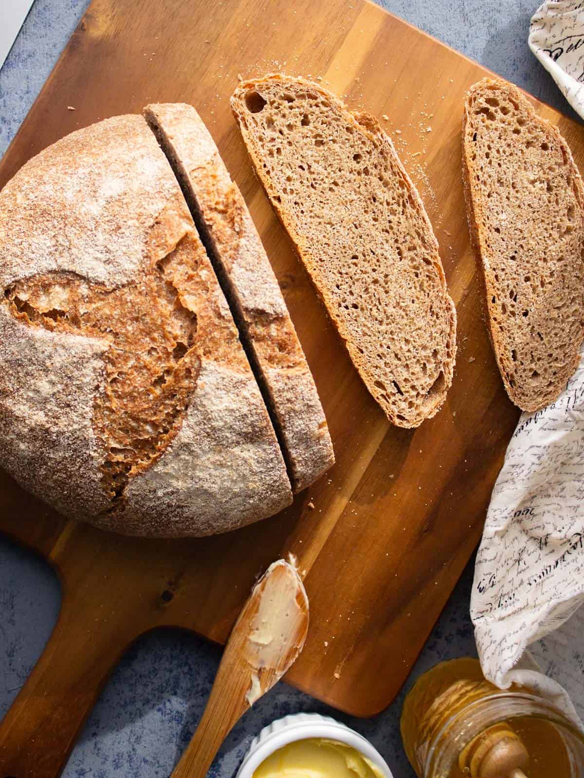 A loaf of rustic whole wheat bread on a cutting board with a couple slices next to it.