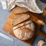 A loaf of rustic whole wheat bread on a cutting board with a couple slices next to it.