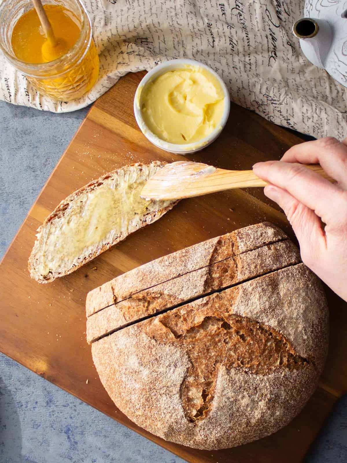 Spreading butter and honey on a slice of rustic whole wheat bread.