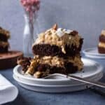 A slice of German chocolate cake on a plate with a fork full of cake next to it.