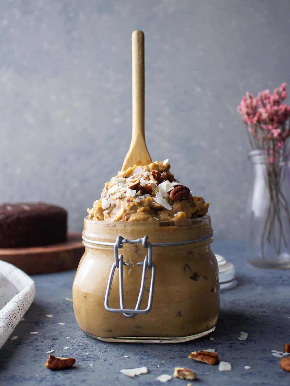 A glass jar filled with coconut pecan frosting with a spoon stabbed in the top.