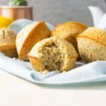 A pile of lemon poppy seed muffins with a bite taken out of one.