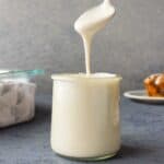 A spoon scooping cream cheese drizzle out of a jar.