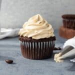 A chocolate cupcakes with a pimple of light brown frosting piped on top.