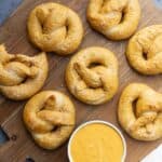 Baked soft whole wheat pretzels on a wooden board with a dish of cheese sauce.