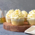 Cupcakes sitting on a wooden cake platter with frosting piped on top.