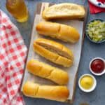 Whole wheat hot dog buns spread out on a wooden board.