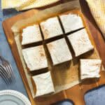 Slices of pumpkin bars frosted with cream cheese frosting on a wooden board.
