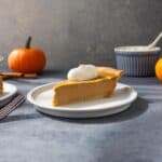 A slice of pumpkin pie on a plate with a dollop of whipped cream on top.
